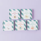 Five 'Cross Stitch Kit' boxes arranged in two rows on a light lavender background. The boxes feature a white and teal diagonal striped border with vintage-style illustrations and text for different cross stitch patterns.