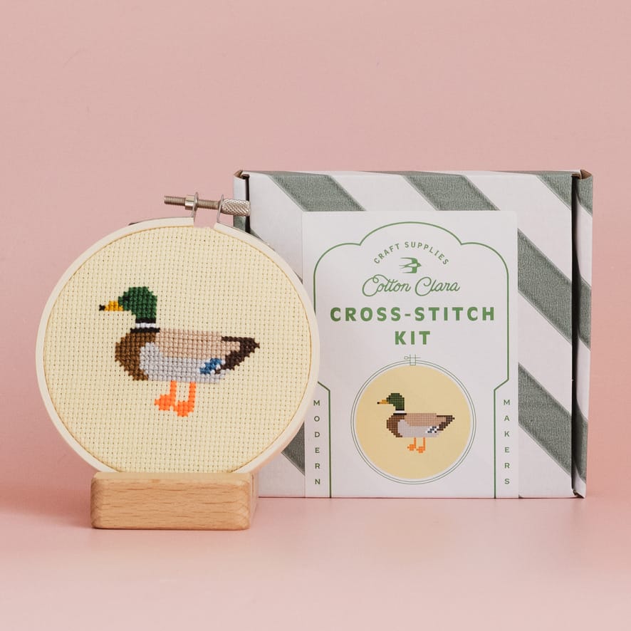 Cross-stitch kit with a completed duck design on a pink background